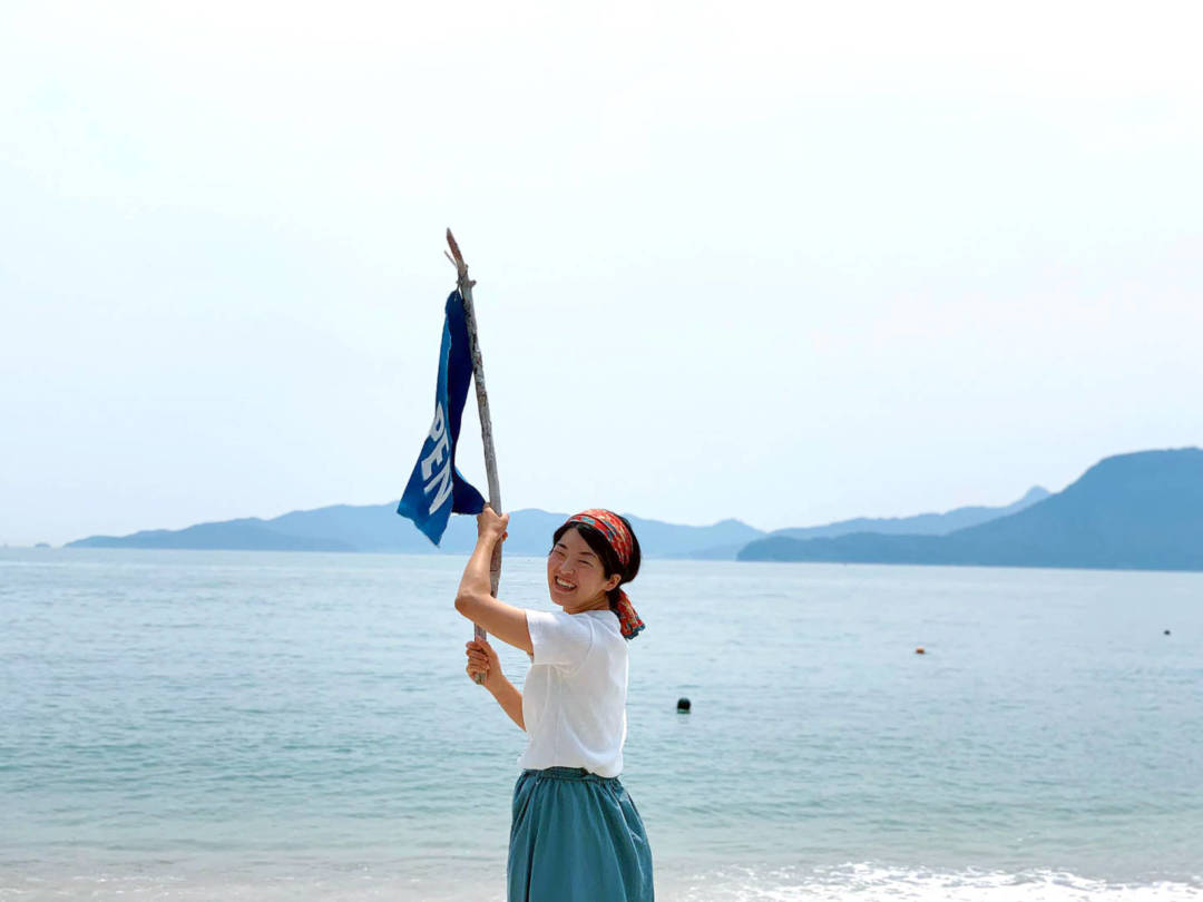 店長目加田怜美面對大海搖動自製「open」旗幟。