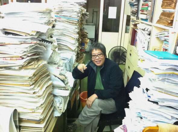 小毅在華僑報的書桌上，堆滿了紙張和舊報紙。